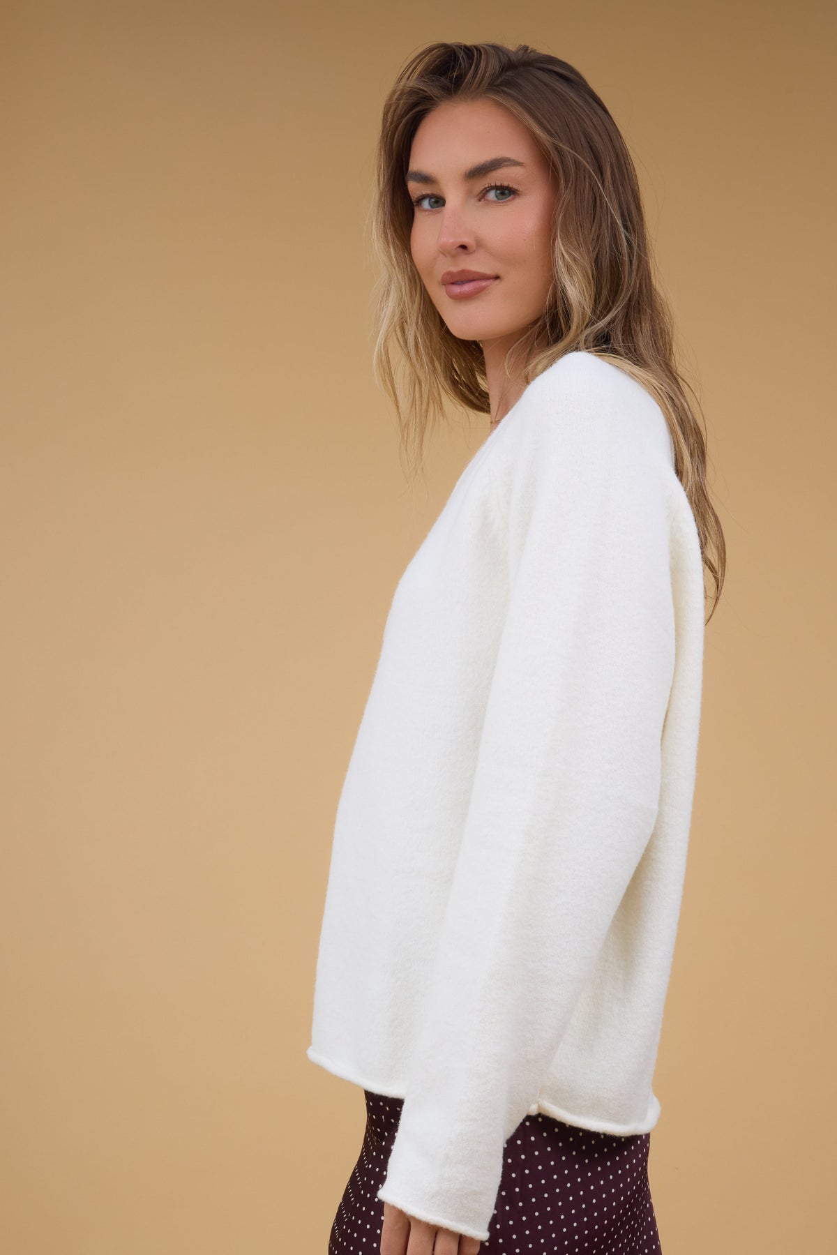 Side view of a woman wearing a cream loose fitting sweater with long sleeves.