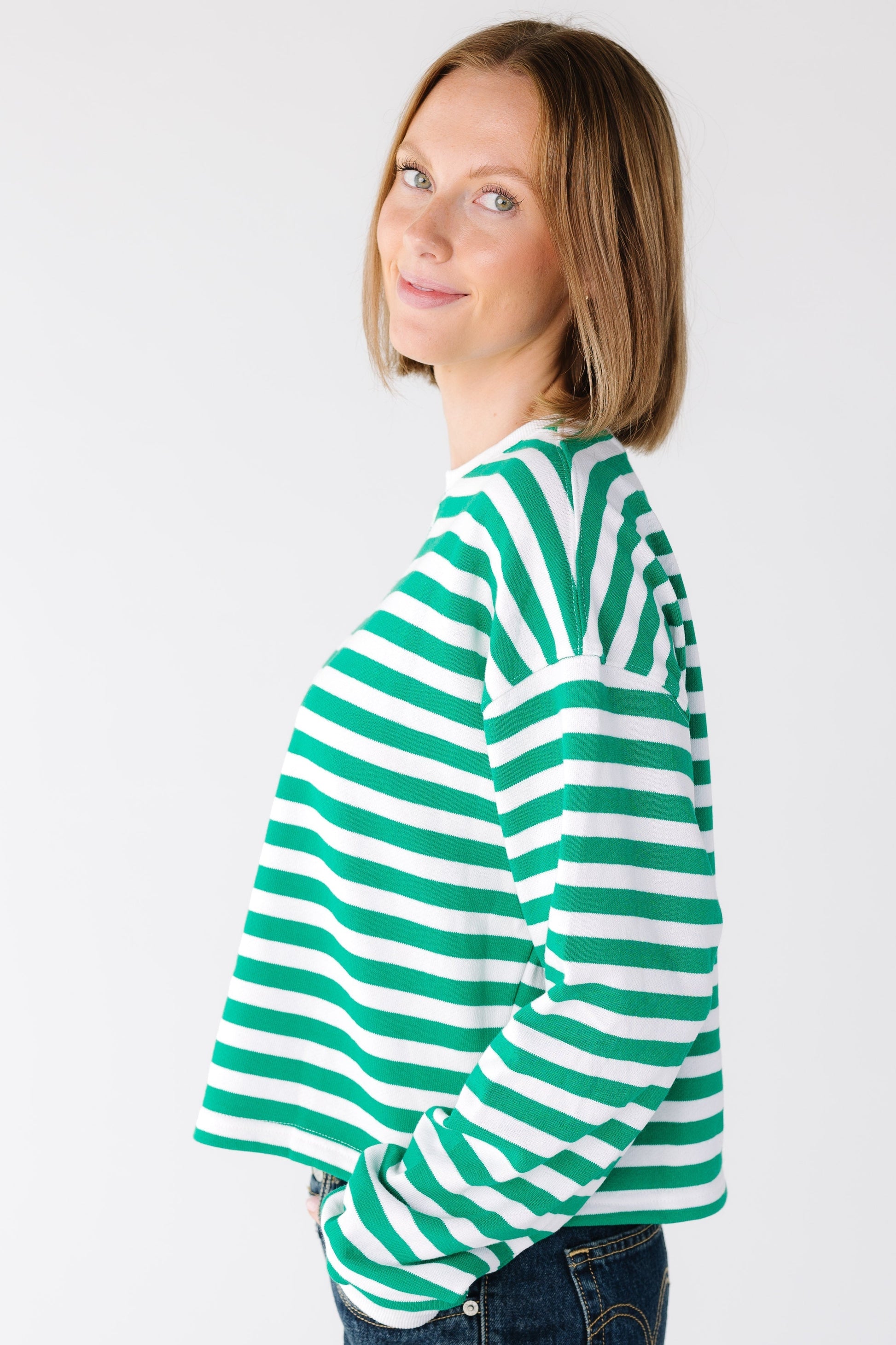Side view of a woman wearing a green and white stripe top with a drop shoulder and long sleeves