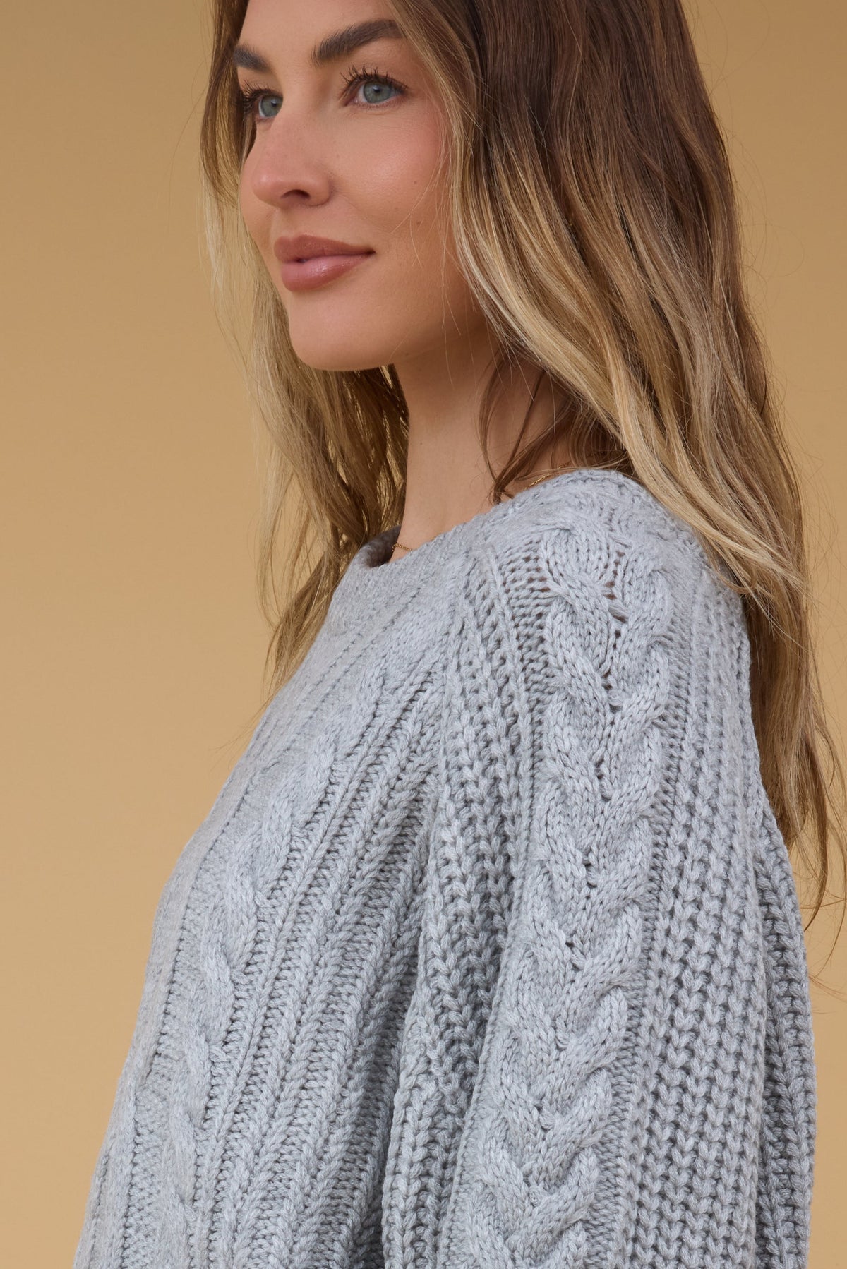 Close side view of a young woman wearing a cable knit grey sweater.