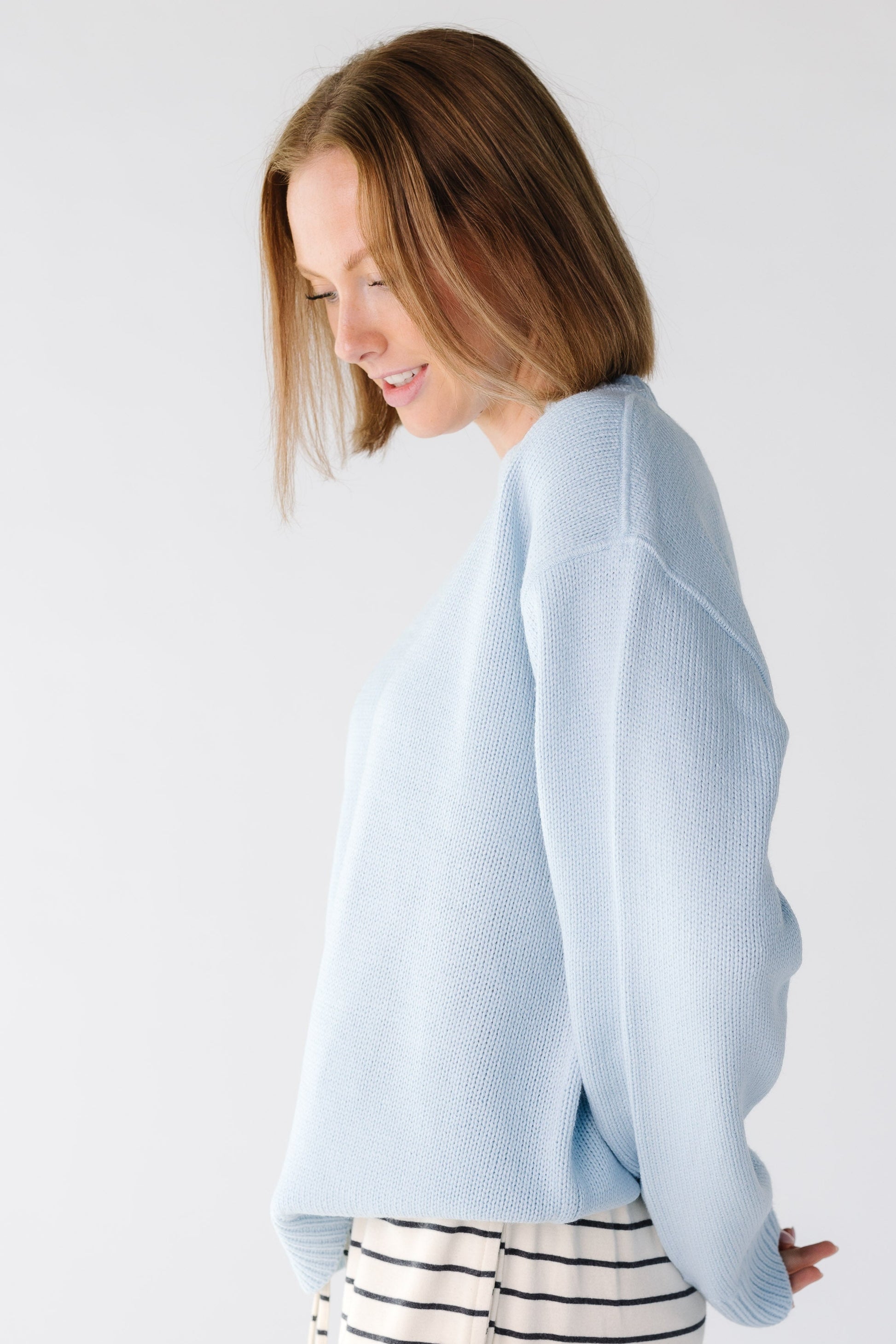 Side view of a woman wearing a light blue sweater with long sleeves