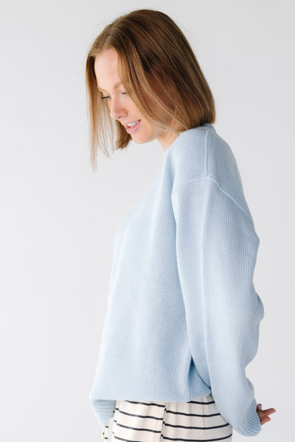 Side view of a woman wearing a light blue sweater with long sleeves