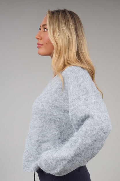A side view of a woman wearing a grey fuzzy sweater with drop shoulders and long sleeves.