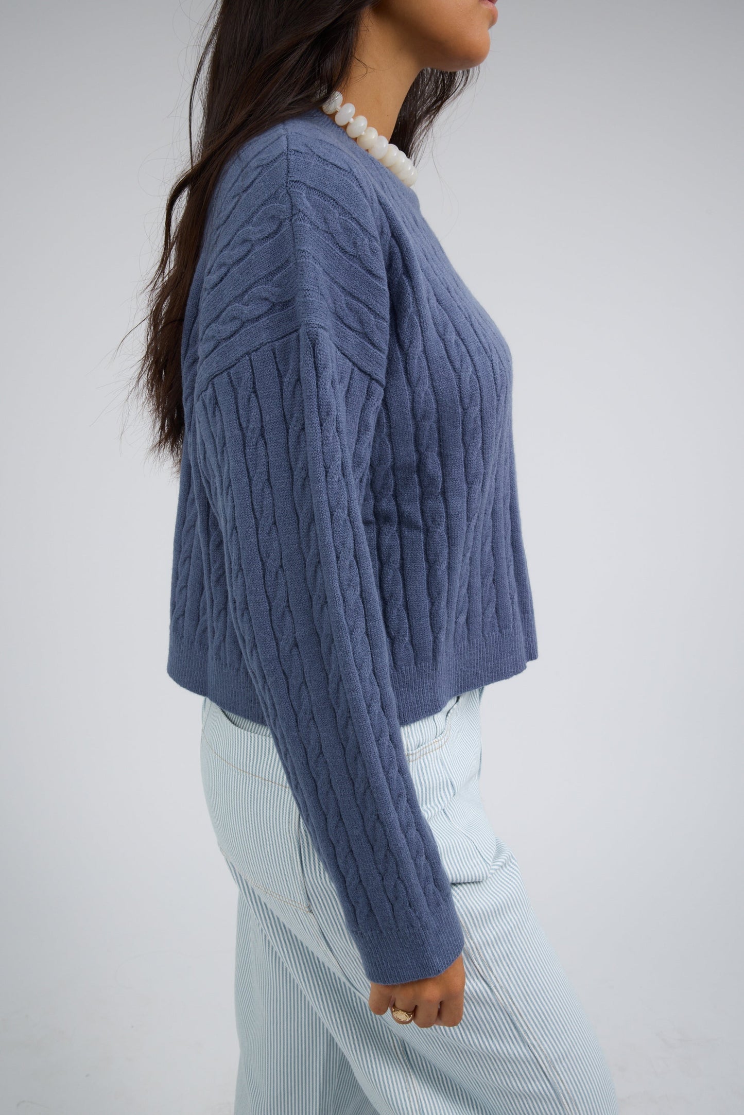 Side view of a woman wearing a modest cable knit, long sleeves sweater.