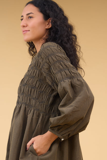 Close view of a woan wearing a brown & black gingham dress with spaced smocking stripe and long sleeves.
