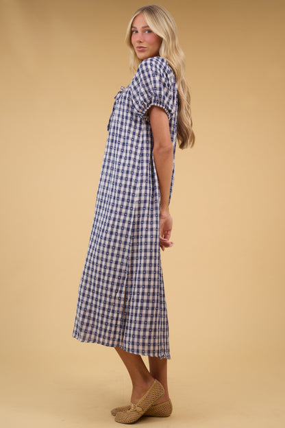 Side view of a young woman wearing a loose fitting midi dress in navy gingham with balloon sleeves.