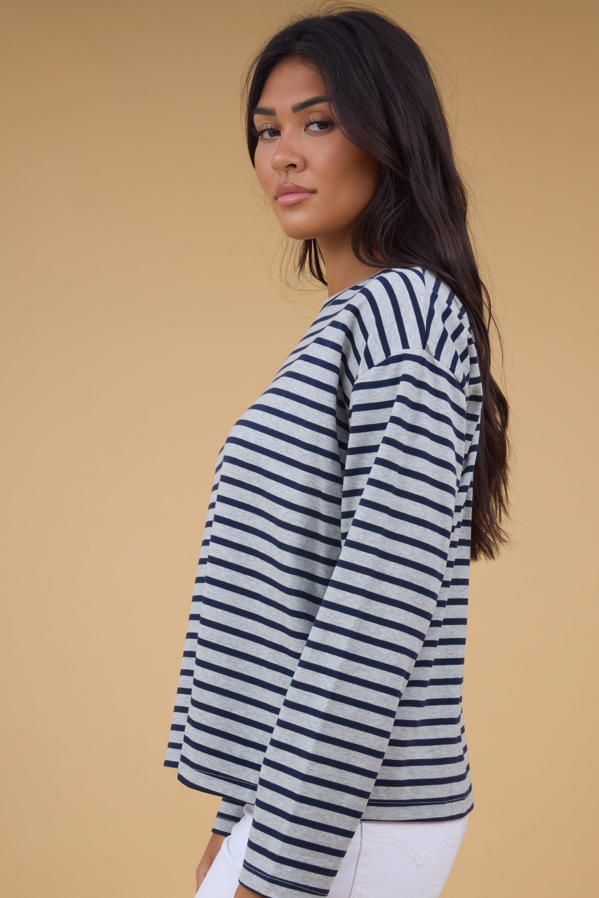 Side view of a woman wearing a grey & navy stripe, long sleeve tee.