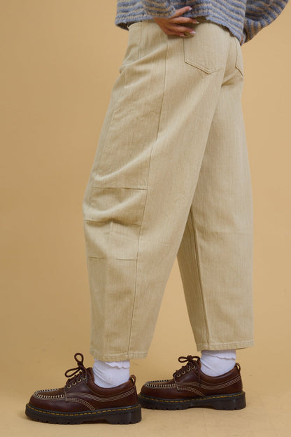 Side view of a young woman wearing wide leg barrel pants in beige.