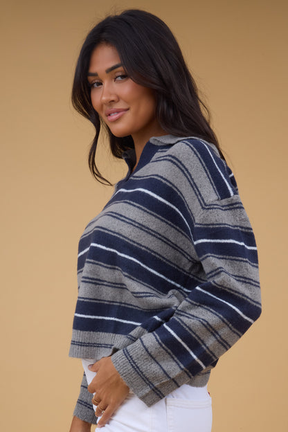 Side view of a woman wearing a grey & navy stripe pullover sweater with long sleeves.
