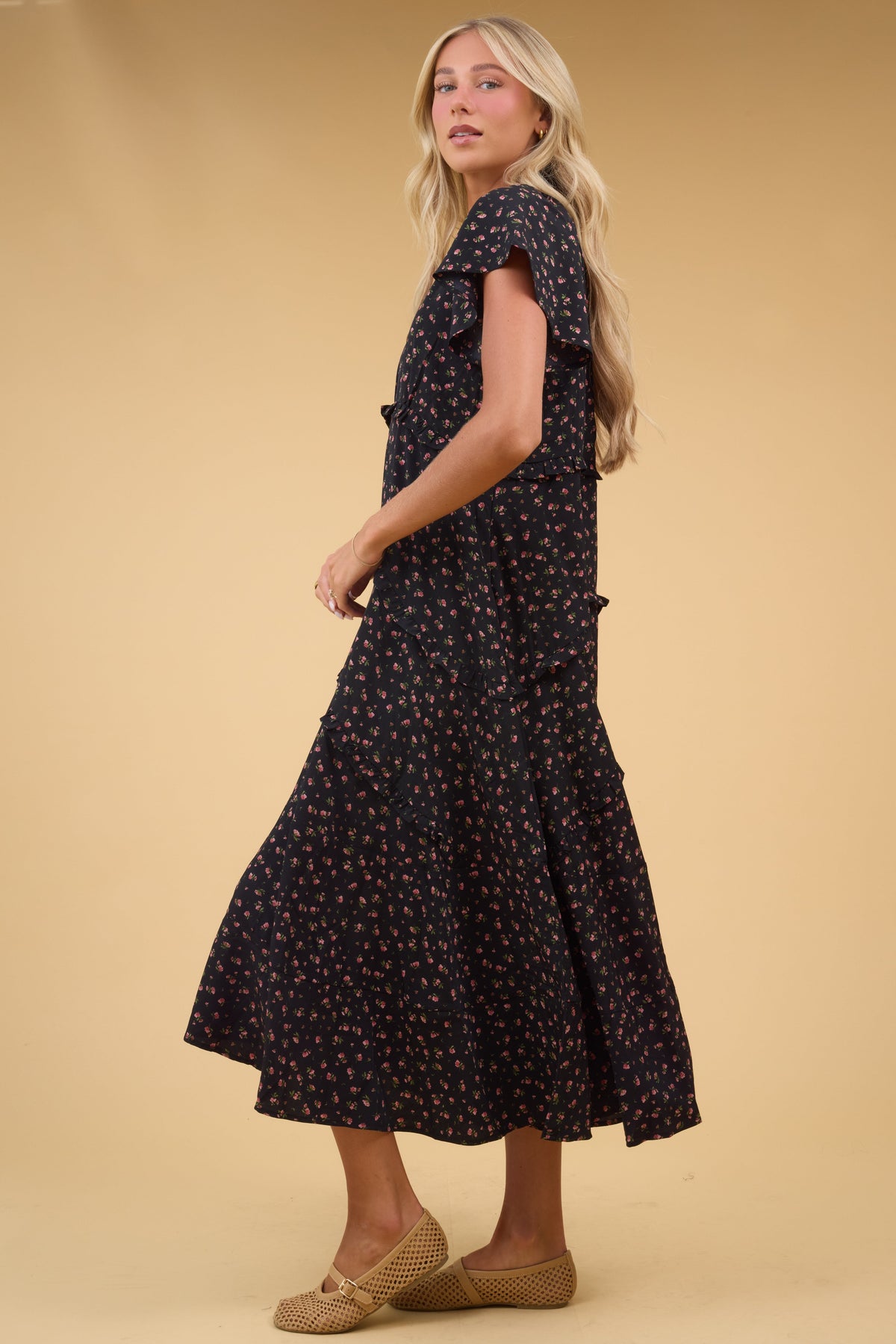 Side view of a woman wearing a loose fitting, flowy dress in black with pink floral print with short sleeves.