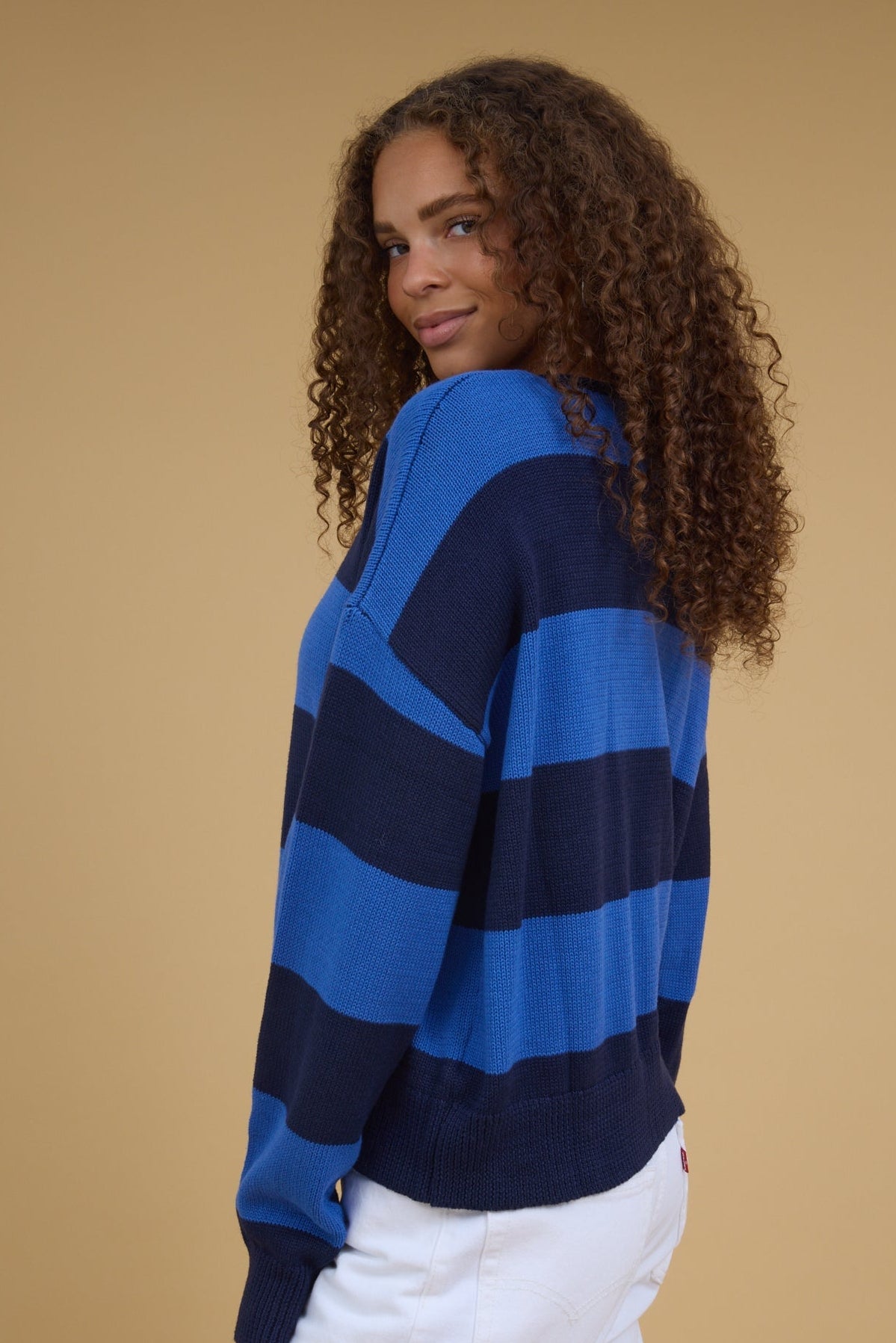 Side view of a woman wearing an oversized blue & navy wide stripe cardigan with long sleeves.