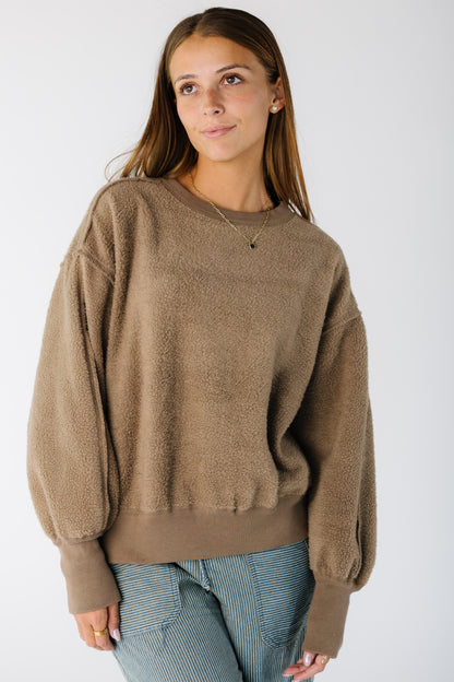 Woman wearing a brown long sleeve sweater-sweatshirt with wide ribbed cuffs