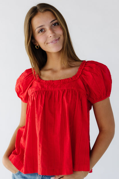 Young woman wearing a modest red baby doll top with a ruffled square neckline and short puff sleeves.