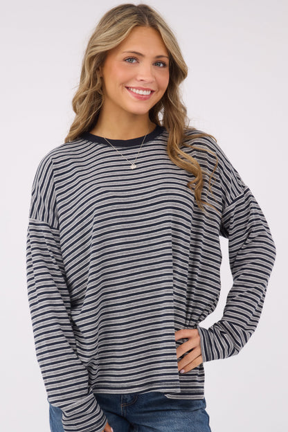 A young woman wearing a modest, loose fitting long sleeve knit top in navy & grey stripe.