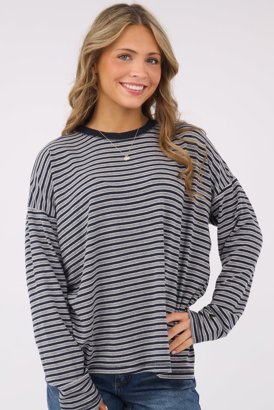 A young woman wearing a modest, loose fitting long sleeve knit top in navy & grey stripe.