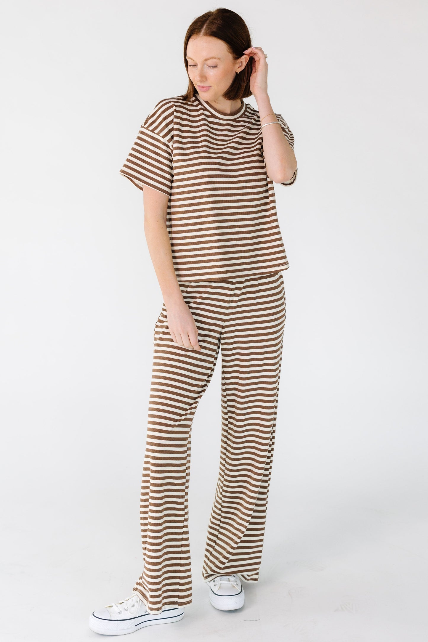 Full view of a young woman wearing a brown and cream loose fitting stripe lounge pant.