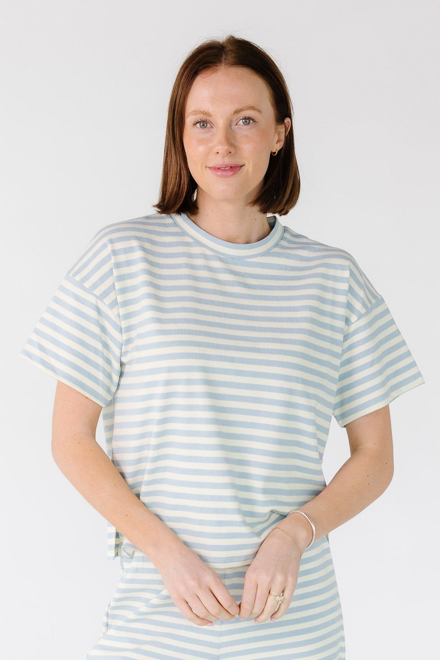 Woman wearing a light blue and white stripe rib knit top with a crew neckline and short sleeves.