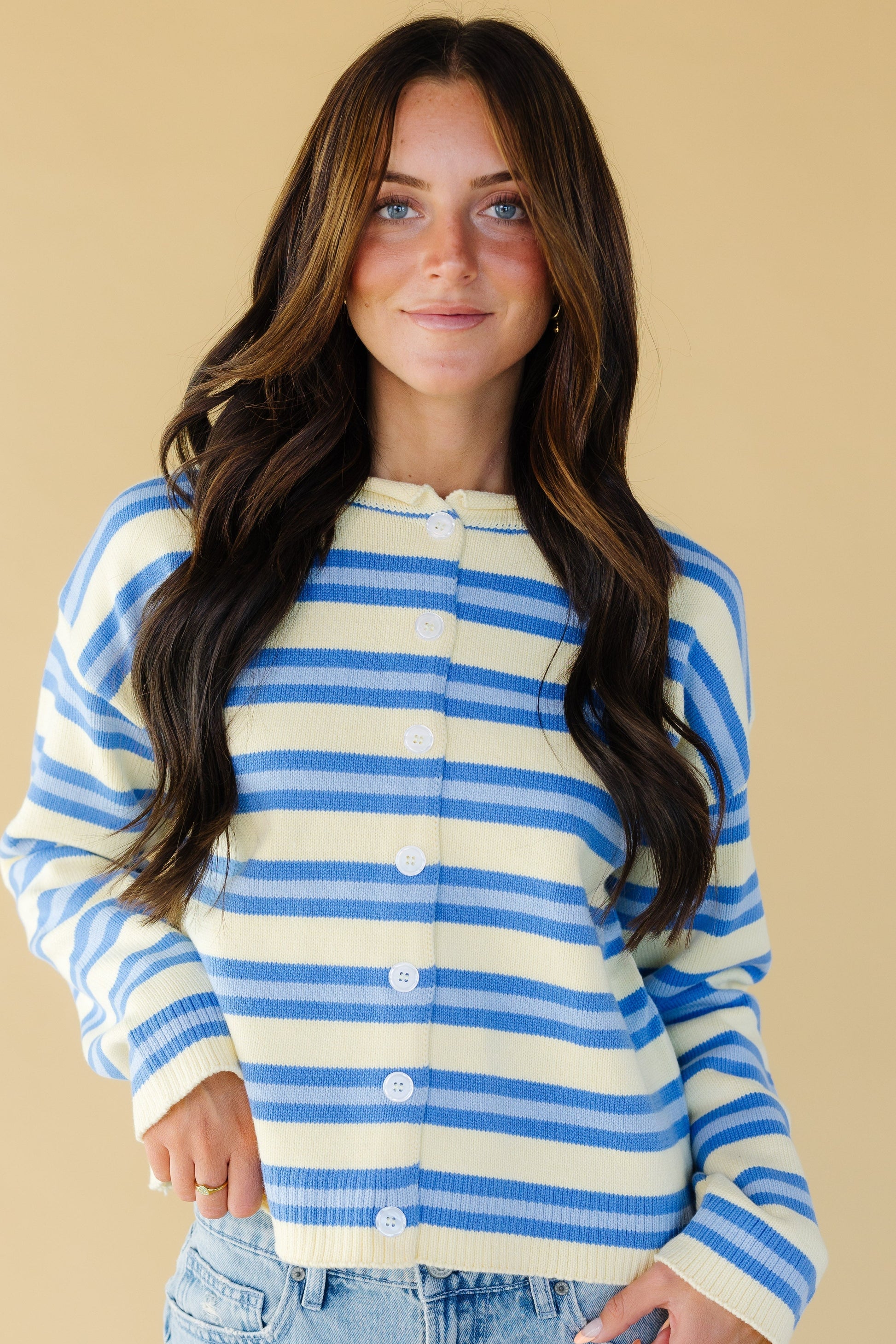 Young woman wearing a yellow & blue stripe button down cardigan with long sleeves.