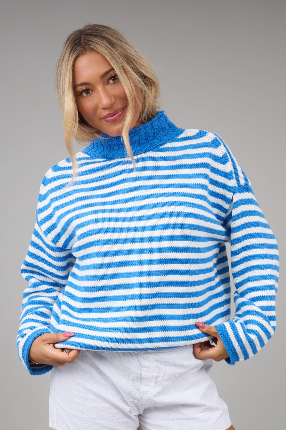 Young woman wearing a blue & white stripe loose fitting sweater with a turtleneck and long sleeves.