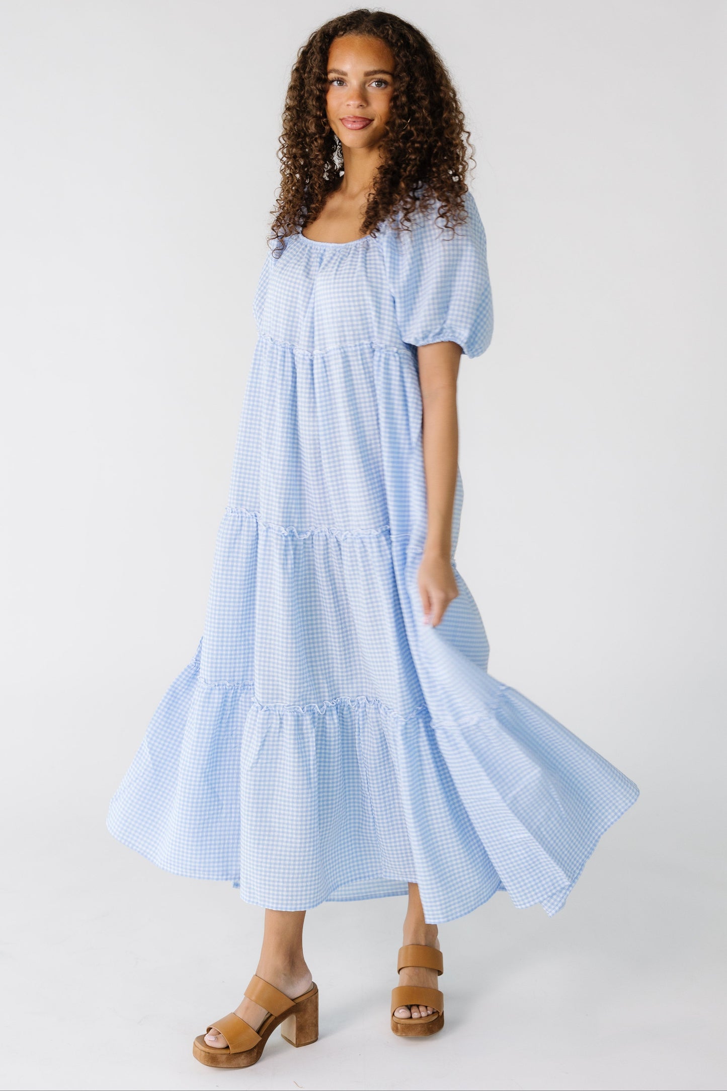 A loose fitting blue gingham tiered dress worn by a teenage girl.