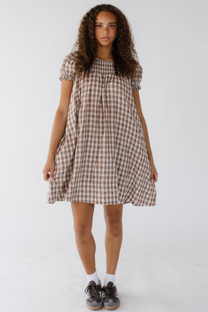 Young woman wearing a brown & white gingham knee dress with puff sleeves and a smocked yoke.