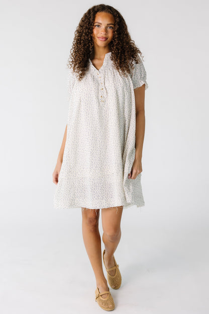 Teen girl wearing a white and grey print short dress with scissor cut hems.