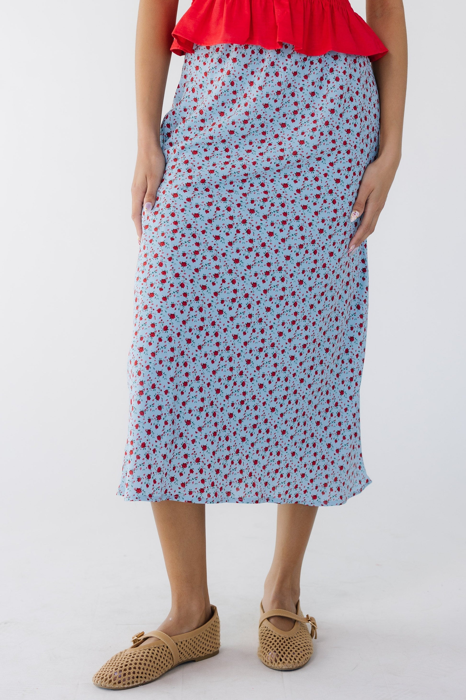 Young woman wearing an A-line midi skirt in light blue with a red floral print.