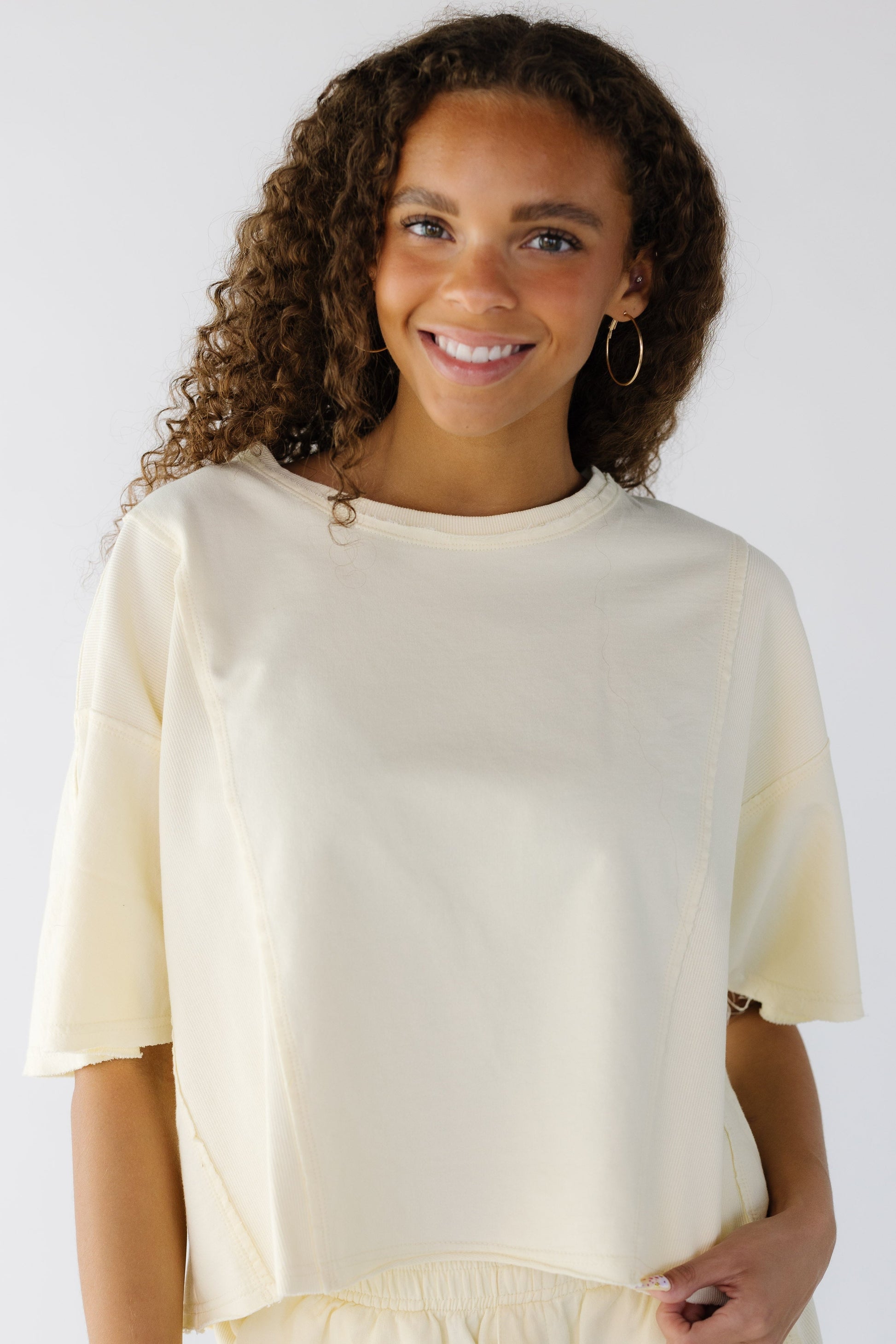 Teenage girl wearing a loose fitting yellow tee with a wide round neckline.