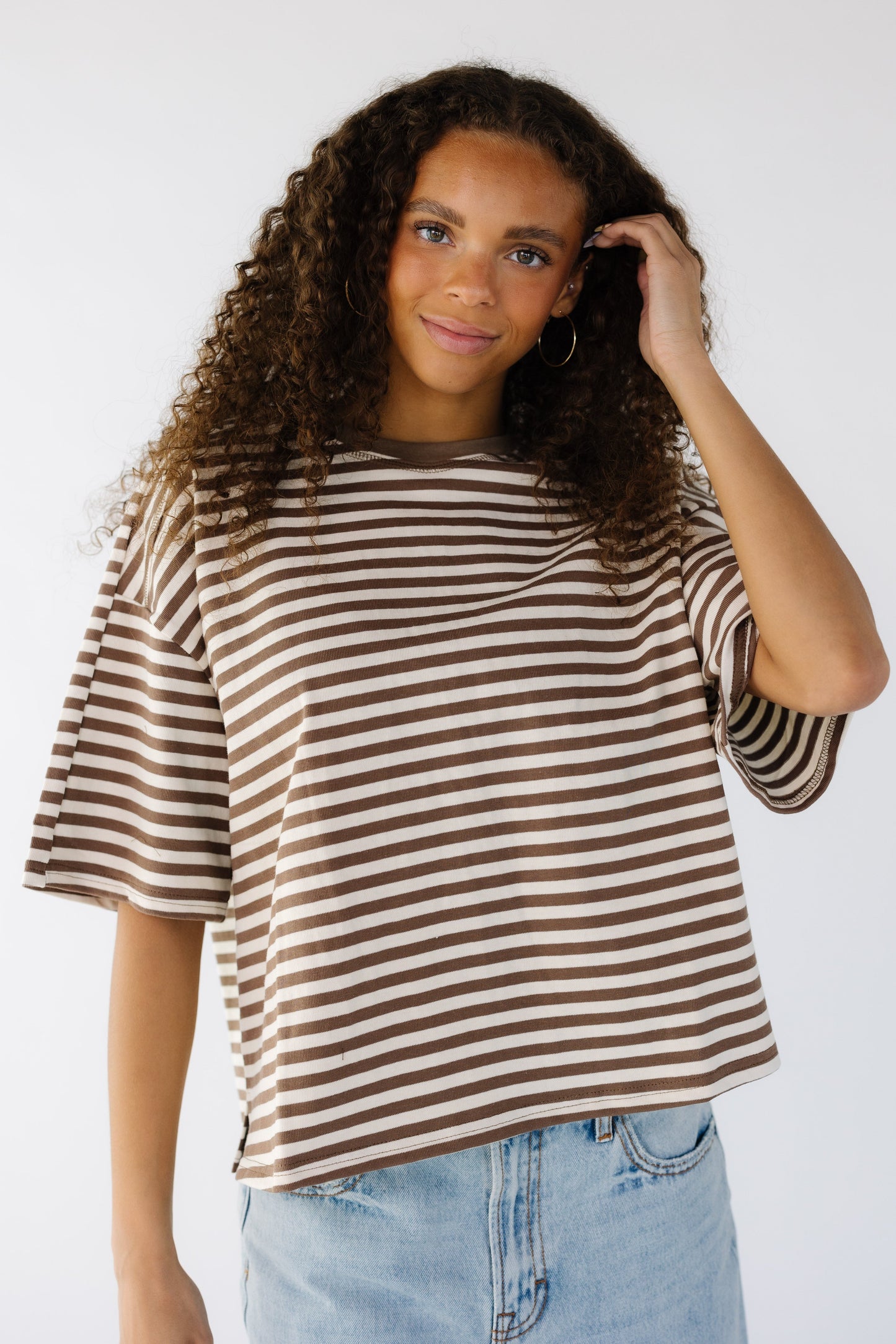 Teenage girl wearing a brown and white loose fitting tee with short sleeves and a crew neckline.