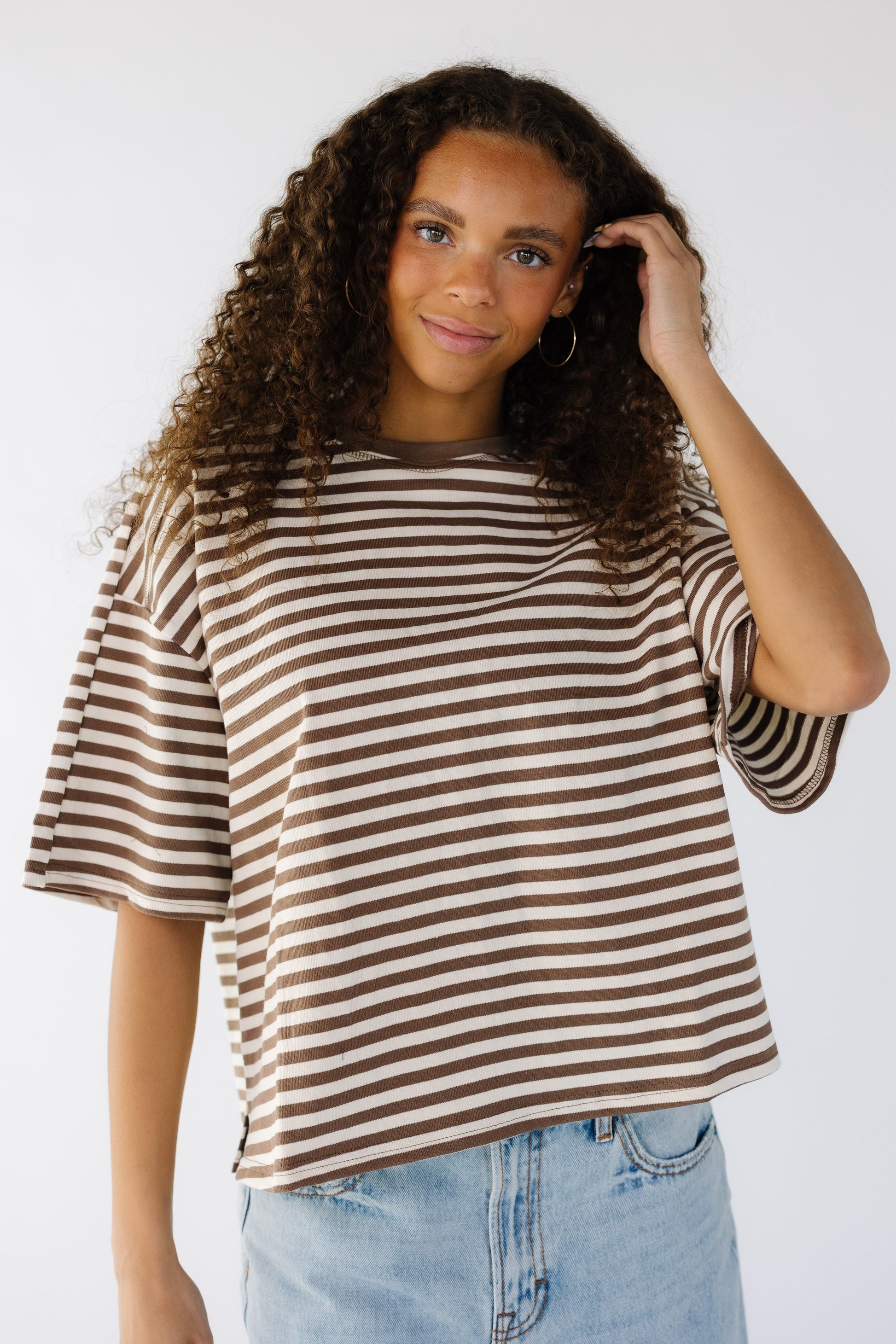 Teenage girl wearing a brown and white loose fitting tee with short sleeves and a crew neckline.