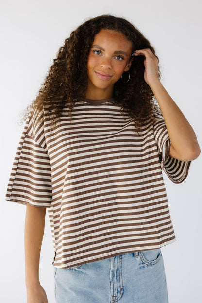 Teenage girl wearing a brown and white loose fitting tee with short sleeves and a crew neckline.