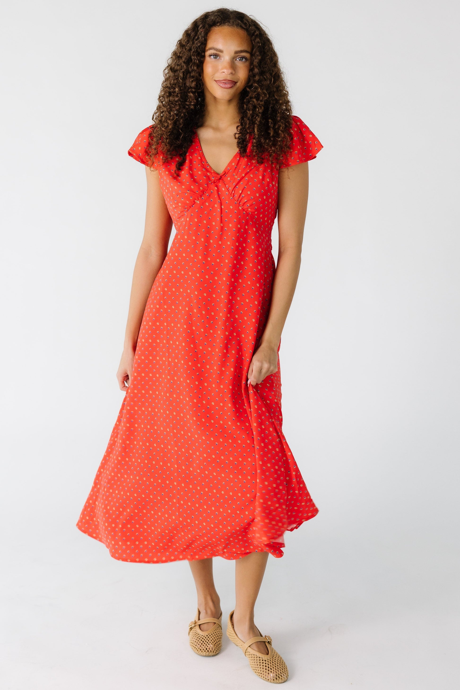 Teenage girl wearing a red midi dress that is closer fitting through the bodice and waist with a flared skirt.