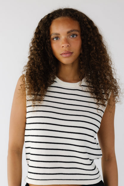 Teenage girl wearing a white and black stripe, sleeveless sweater vest with a crew neckline.