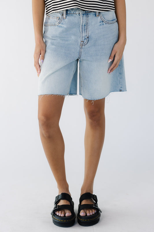 Young woman wearing modest light denim shorts with a loose, wide cut leg and a cut hem.
