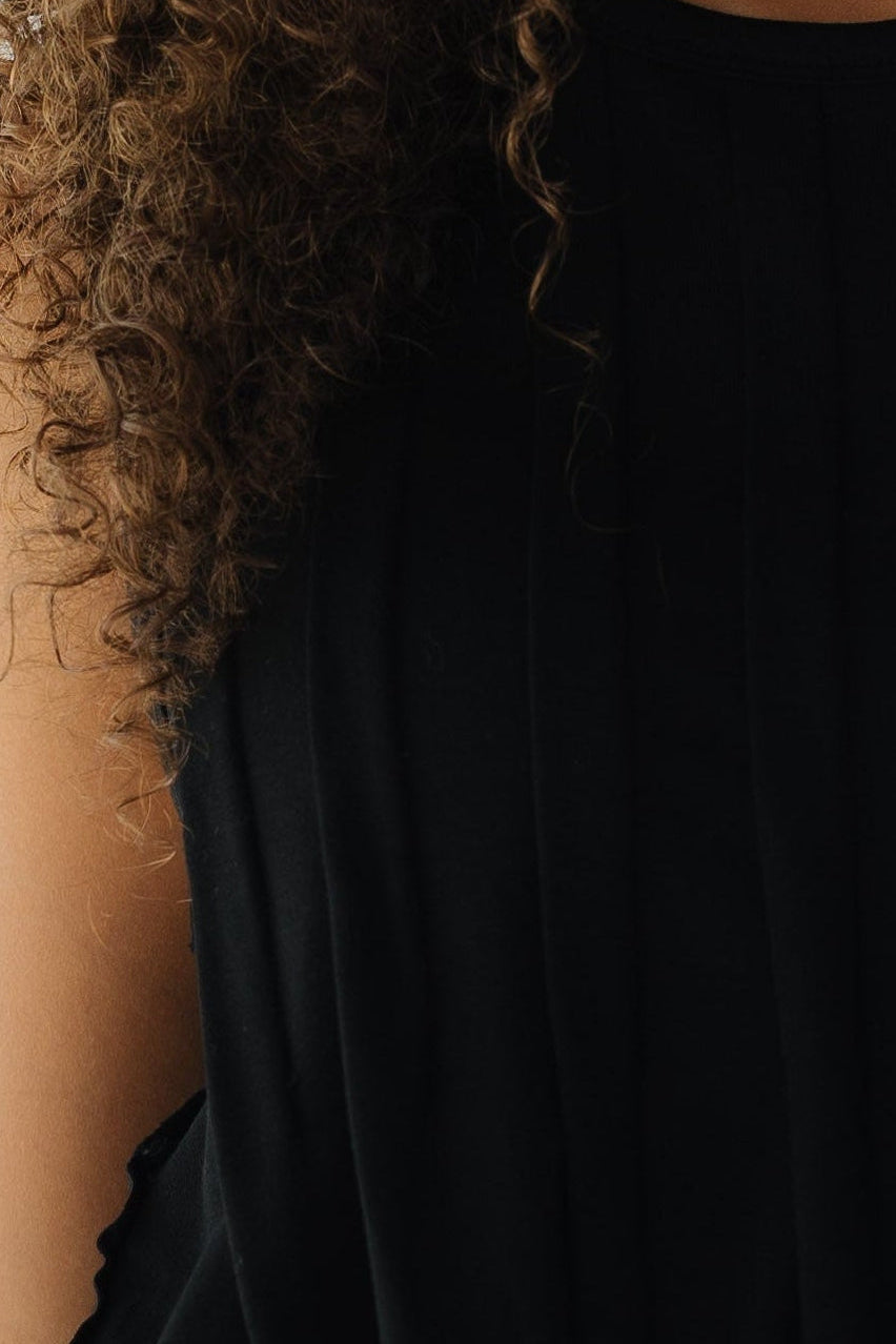 Young woman wearing a sleeveless  black knit top with front pleats.