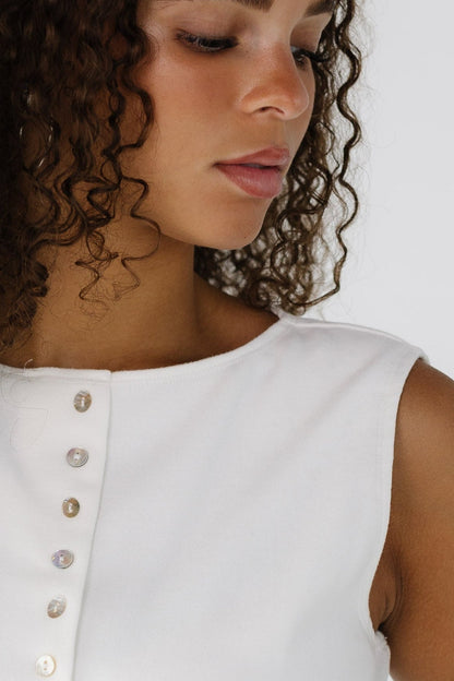 Close view of a teen girl wearing a white sleeveless button down top with a high round neckline.