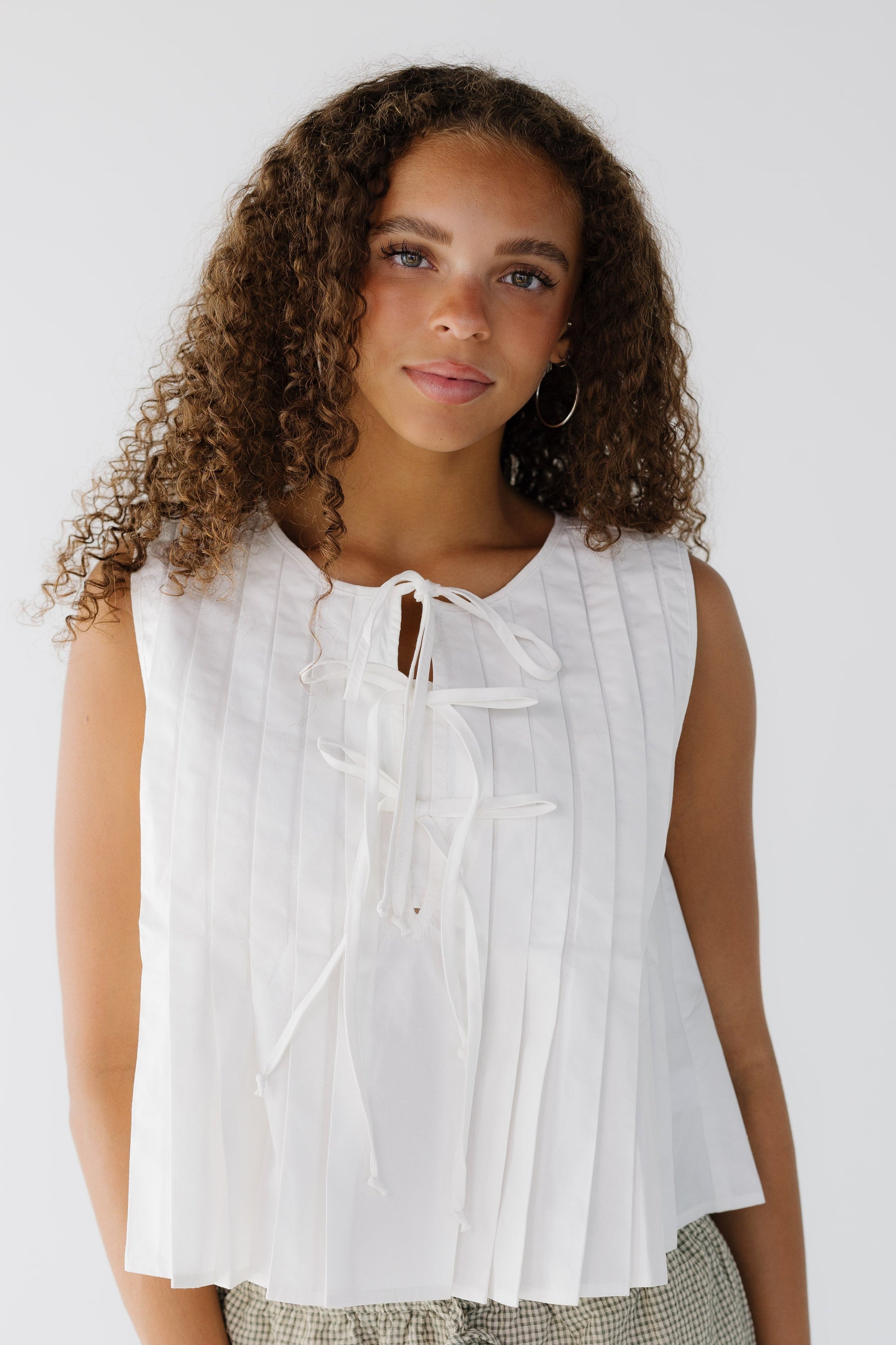 Young woman wearing a white sleeveless pleated blouse with 3 front tie bows.