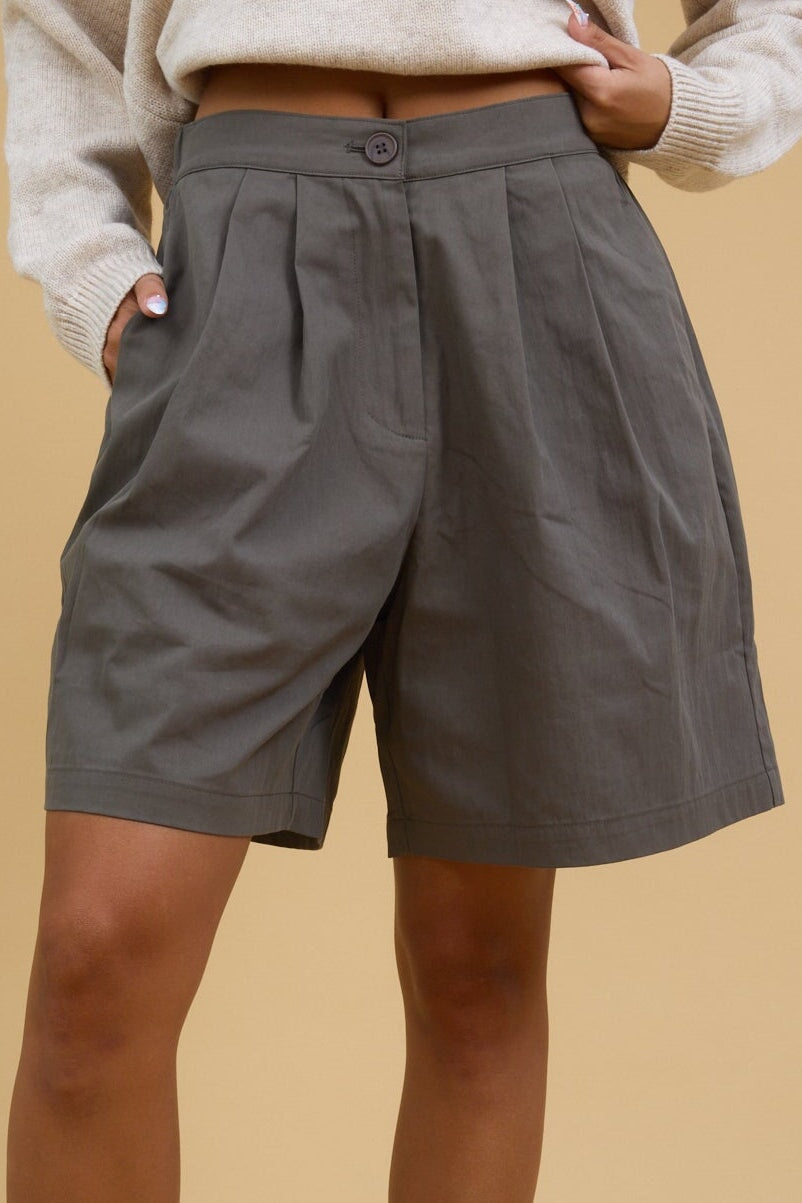 Close view of a young woman wearing pleated trouser shorts with a button & zipper closure.