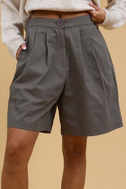 Close view of a young woman wearing pleated trouser shorts with a button & zipper closure.