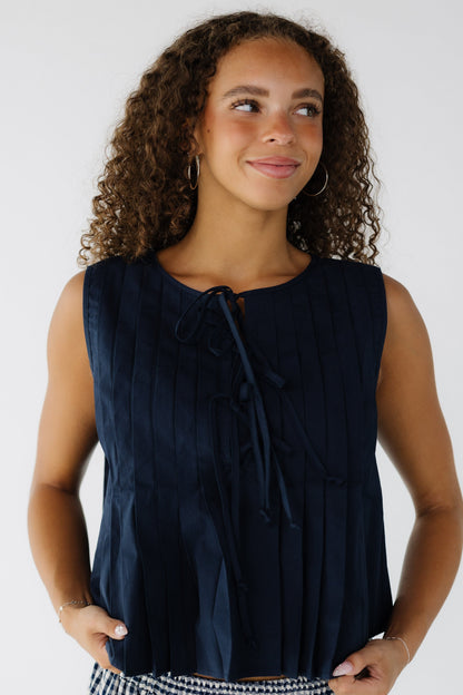Young woman wearing a navy pleated blouse with 3 ties on the front.