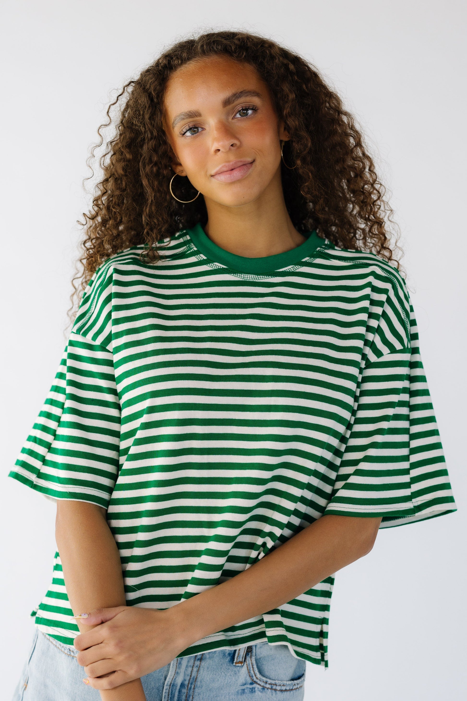 Teen girl wearing a green and white stripe loose fitting tee with short sleeves and a crew neckline.