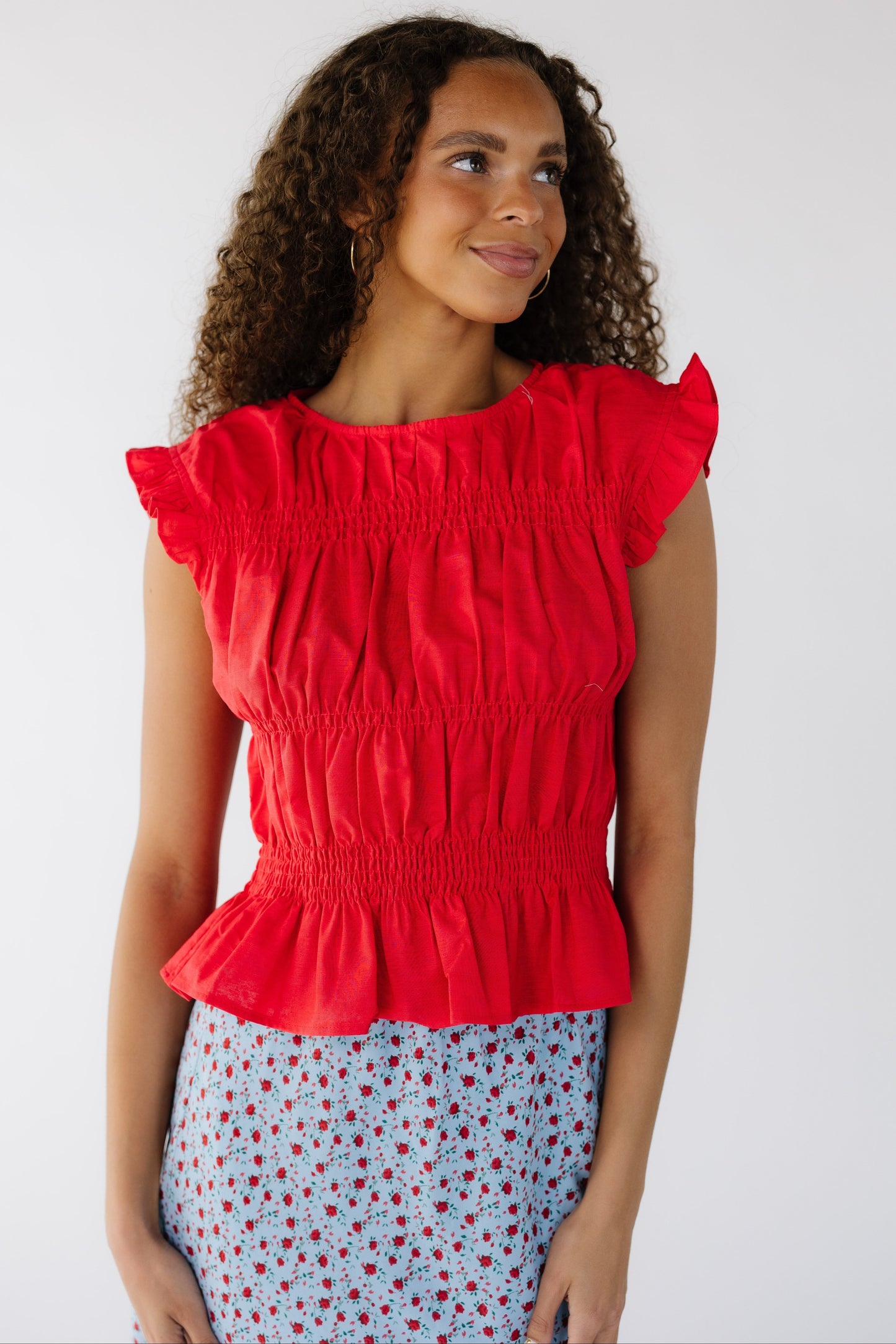 A teen girl wearing a sleeveless  red blouse with rows of smocking.
