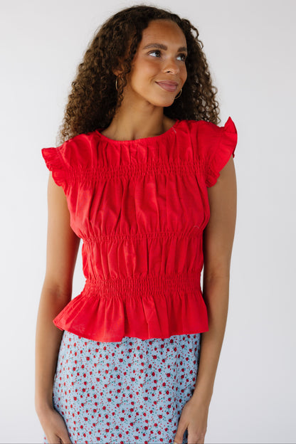A teen girl wearing a sleeveless  red blouse with rows of smocking.