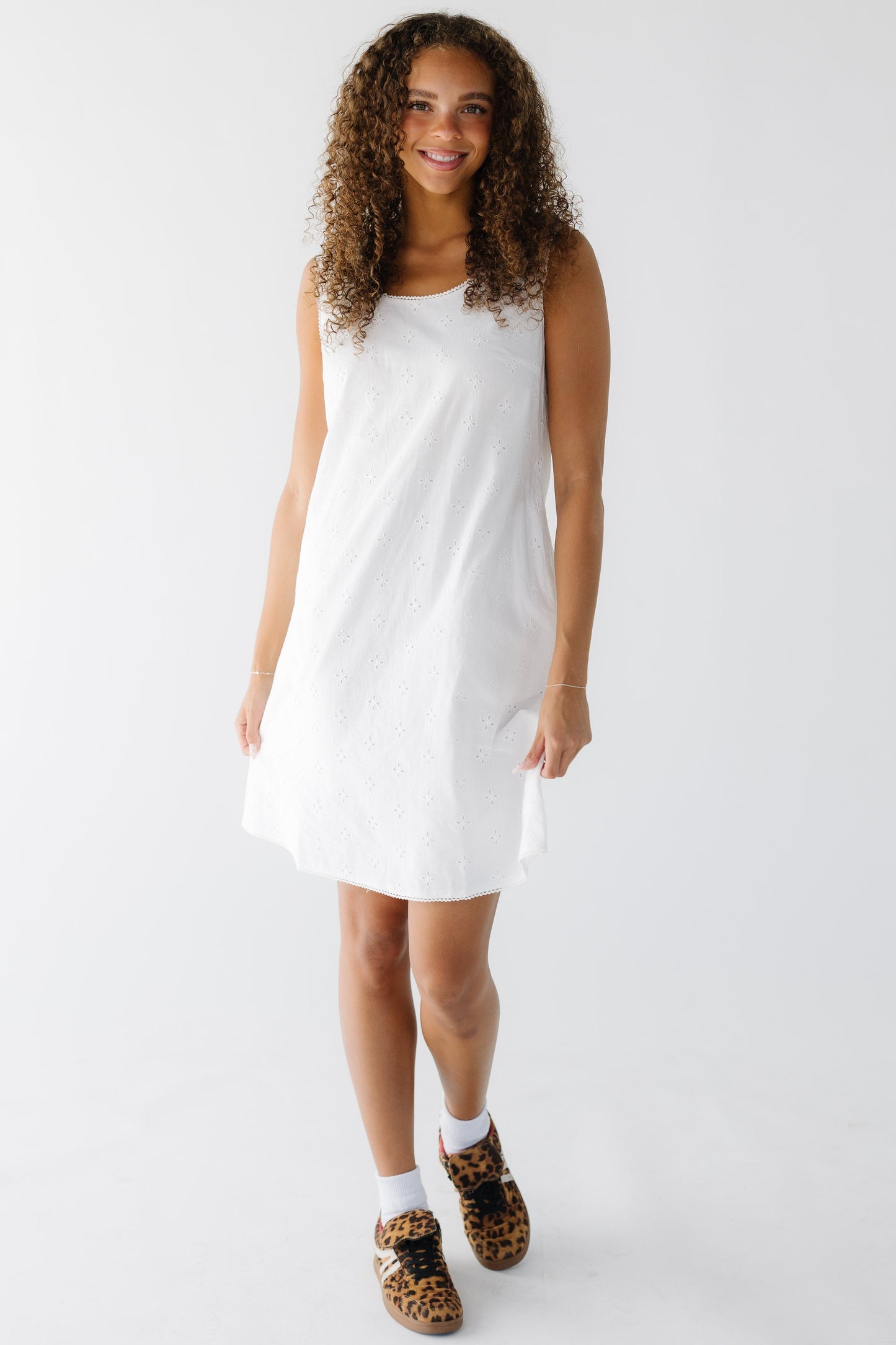 Young woman wearing a sleeveless eyelet shift dress with a scoop neckline.