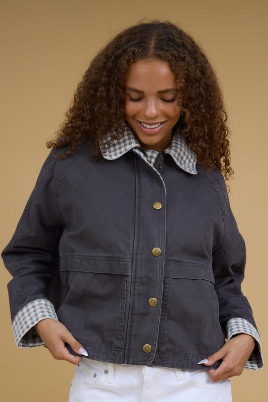 Young woman wearing a modest twill jacket in charoal with gingham cuffs, collar and inside zipper placket.