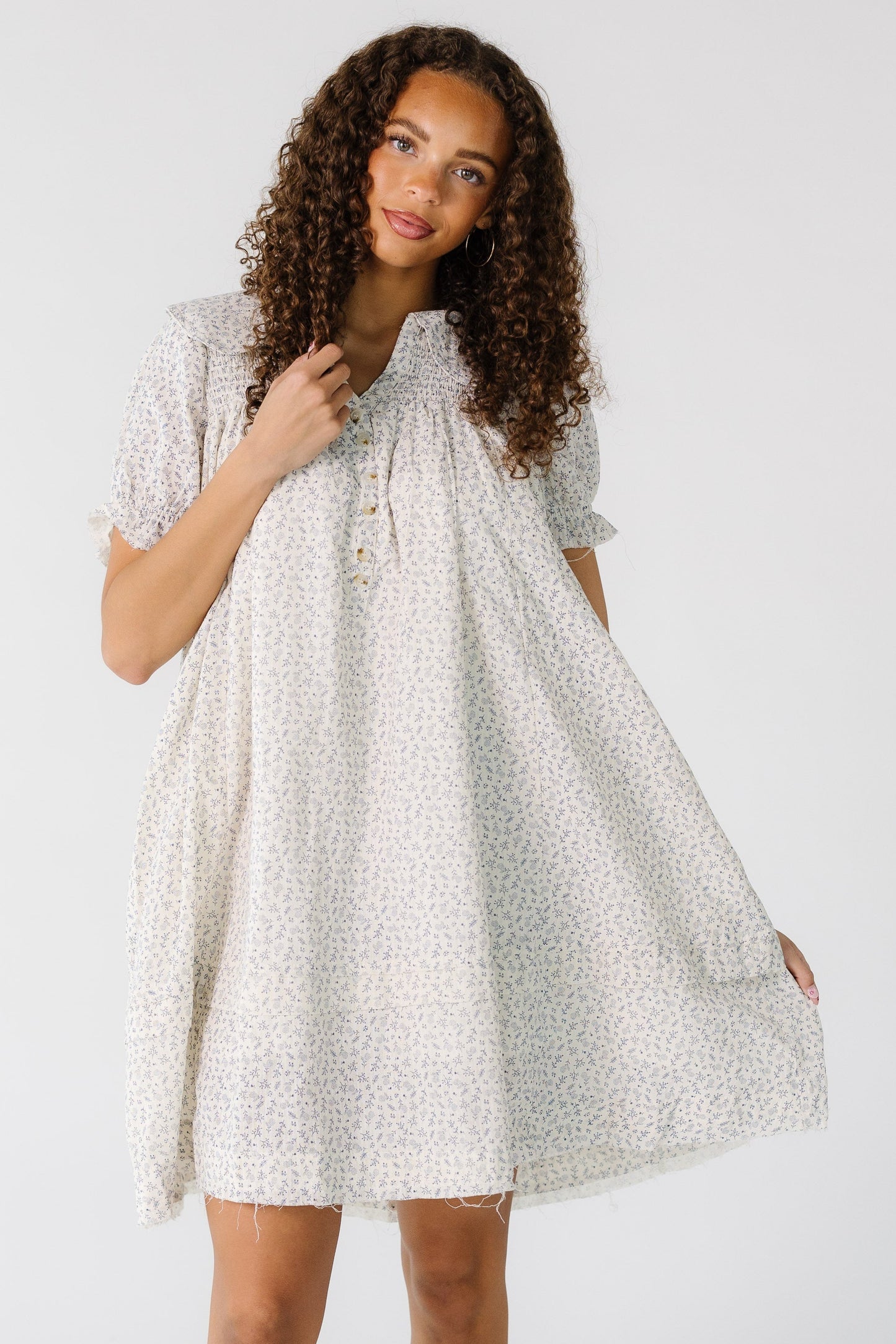 Teen girl wearing a  white and grey print short dress with a V-neckline, short button placket and shot puff sleeves.