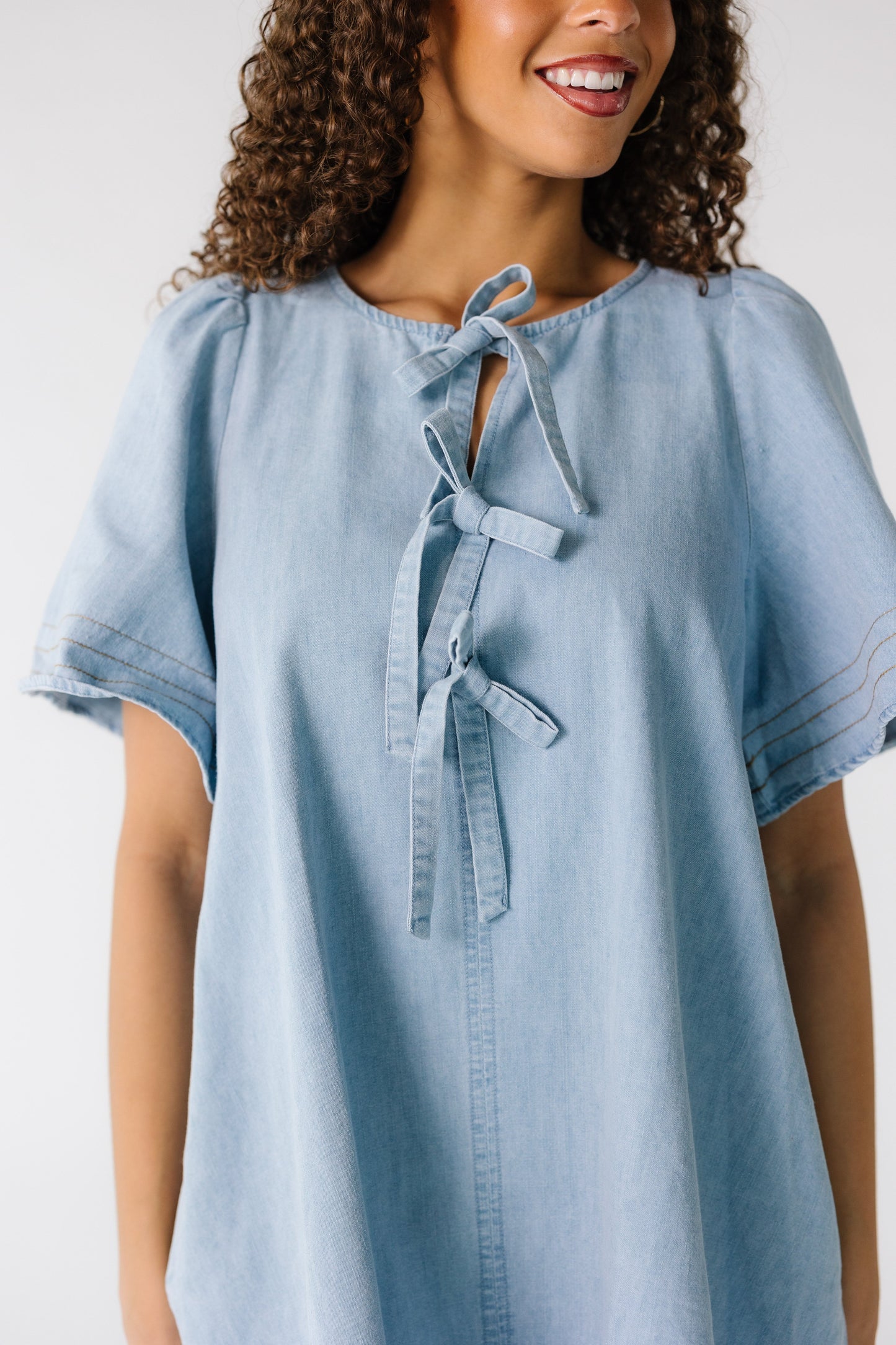 Close view of a woman wearing a light denim dress with 3 tie closure and short sleeves.