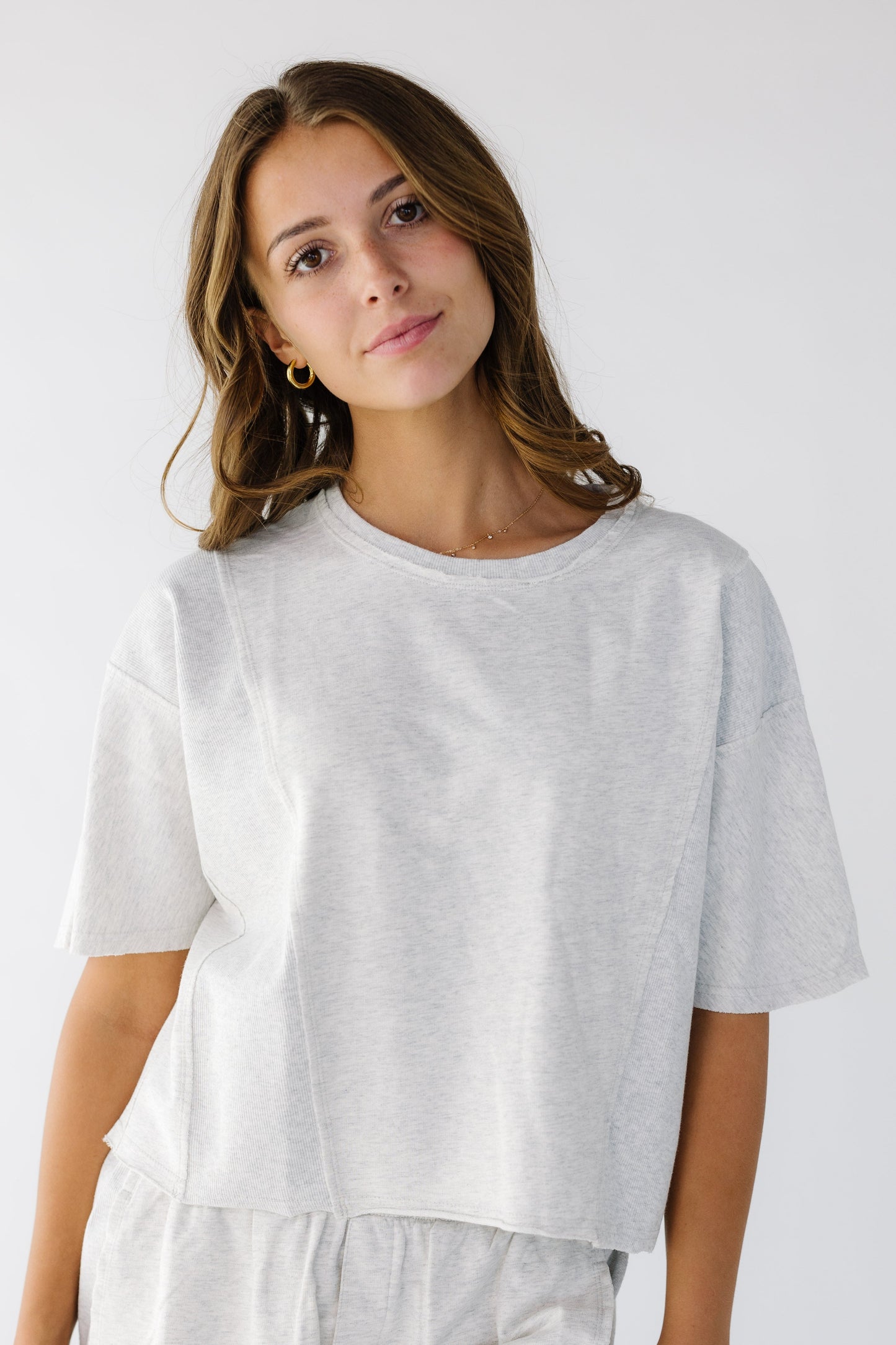 Woman wearing a light grey loose fitting tee with elbow length sleeves and rolled hems.