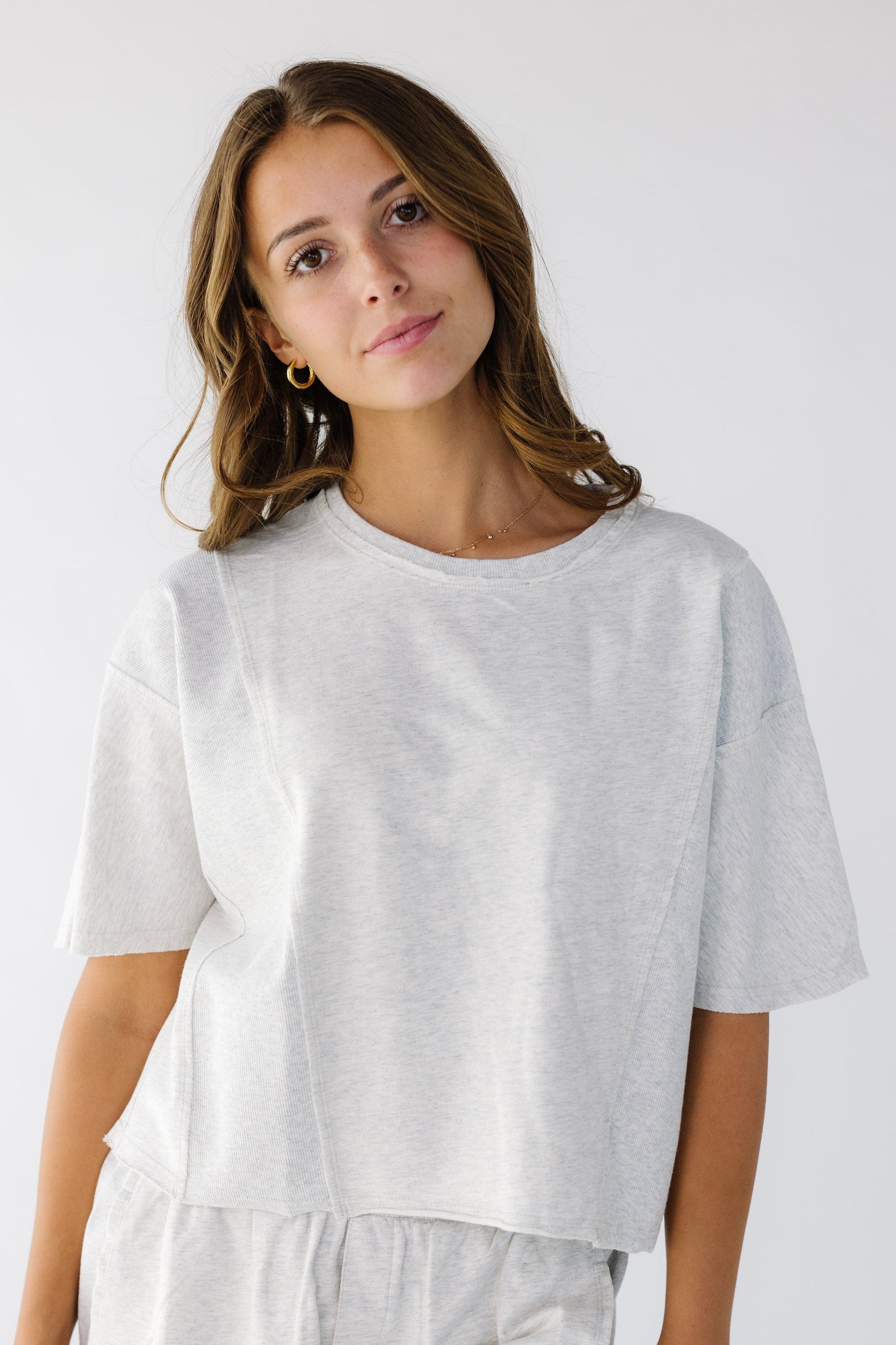 Woman wearing a light grey loose fitting tee with elbow length sleeves and rolled hems.