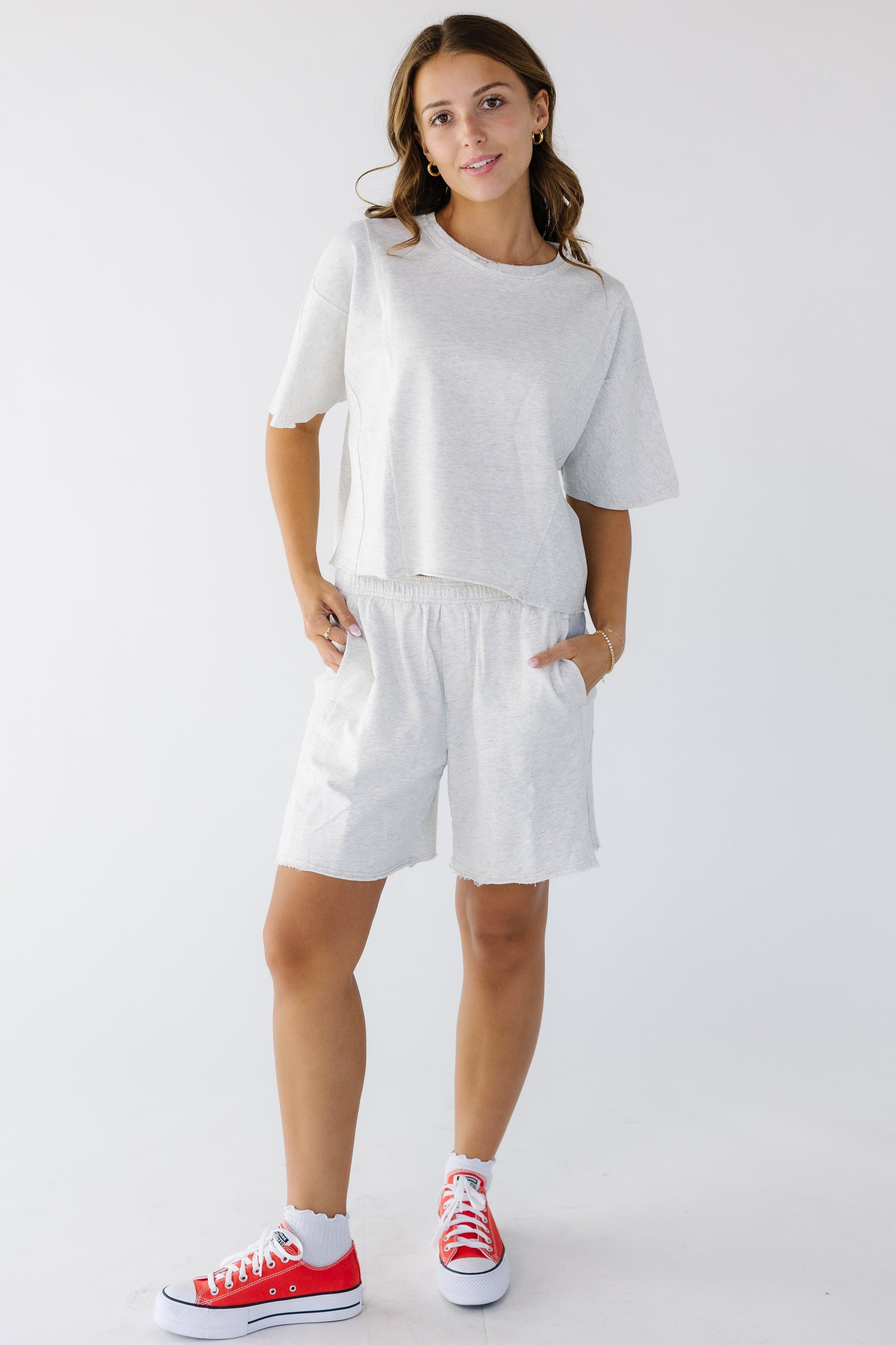 Young woman wearing a light grey loose fitting tee and loose fitting matching shorts.