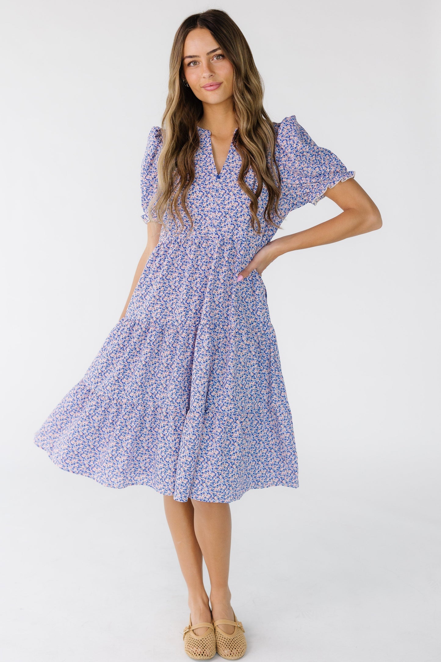 Young woman wearing a purple floral knee length tiered dress with a V-neckline and short puff sleeves.